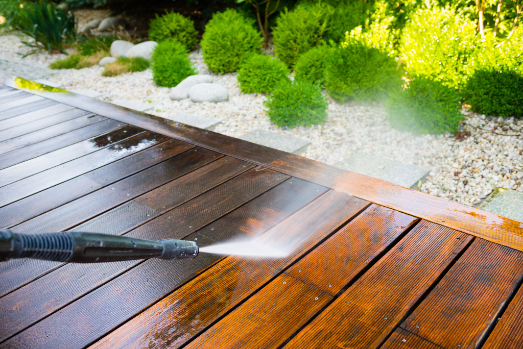 power washer spraying water to clean a wooden deck