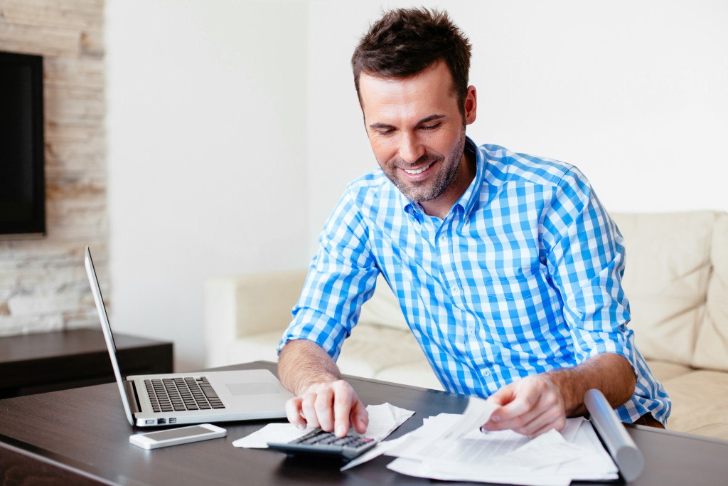 Young man checking his expenses using a calculator and laptop.